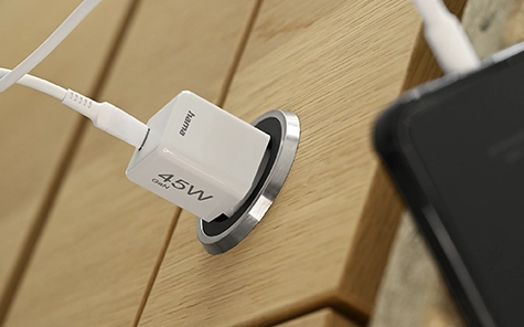 Le chargeur de 45 watts est branché à une prise murale en bois et recharge un smartphone.